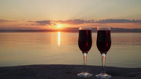 Two glasses of red wine stand on the shore of a lake at sunset. Video stock 252660770