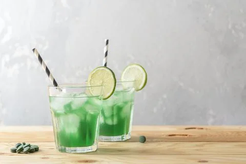 Two glasses of refreshing lemonade with chlorella and lime on a wooden table. Photos