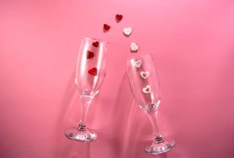 Two glasses with splash of red and white heart on a pink background. Stock Photos