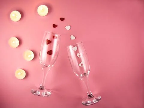 Two glasses with splash of red and white heart and candles on a pink background. Stock Photos