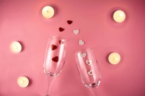 Two glasses with splash of red and white heart and candles on a pink background. Stock Photos