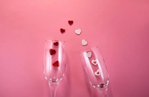 Two glasses with splash of red and white heart on a pink background. Stock Photos