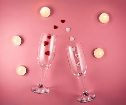 Two glasses with splash of red and white heart and candles on a pink background. Stock Photos