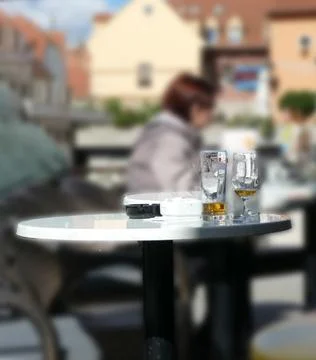 Two glasses standing on table outside cafe with woman sitting in background Stock Photos