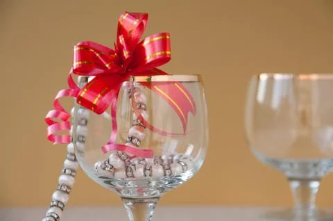 Two glasses, string of pearls and red gift bow on gold background Stock Photos