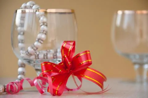 Two glasses, string of pearls and red gift bow on gold background Stock Photos