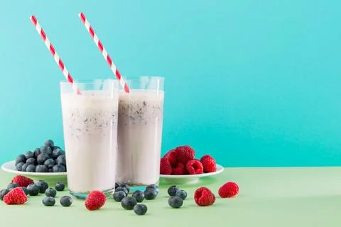Two glasses of thick drinks with red and white straws sit on a green table .. Stock Photos