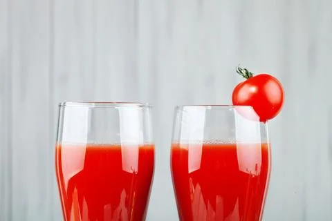 Two glasses with tomato juice and a small tomato on a bright background. Stock Photos