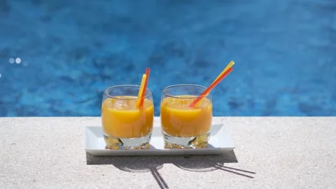 Two glasses with tropical orange juice with ice on swimming pool background. Stock-Footage 243994953