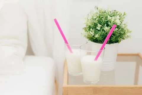 Two glasses of vanilla milkshake on bedside table for breakfast, vase of gree Foto stock