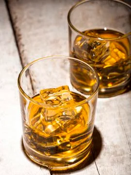 Two glasses of whiskey with ice cubes served on white wooden planks. Stock Photos