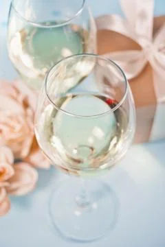Two glasses with white grape wine with roses and gift box on the background.  Stock Photos