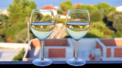 Two glasses with white wine close-up, beautiful white houses with tiled roof Stock Footage 124701889