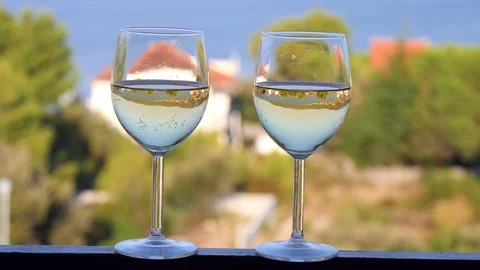 Two glasses with white wine close-up, beautiful white houses with tiled roof Stock Footage 124701927
