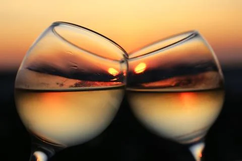 Two glasses with white wine on sunset background, sun reflected in misted glass Stock Photos