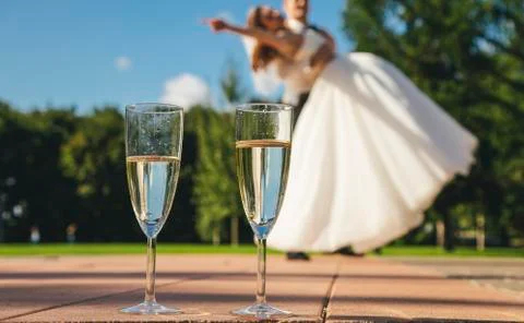 Two glasses with wine on the background of the blurred danced bride and groom. Stock Photos