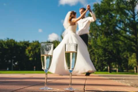 Two glasses with wine on the background of the blurred danced bride and groom. 스톡 사진