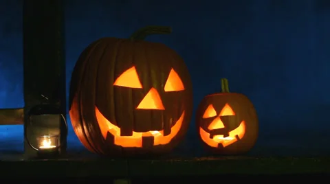 Two glowing jack-o-lanterns and a candle sit on a porch with eerie smoke Stock Footage 30559887