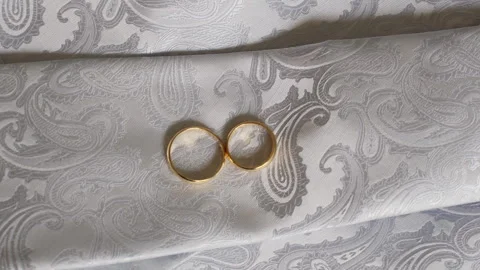 Two Gold Wedding Rings on Elegant Paisley Fabric Symbolizing Love and Commitment 動画素材 324791833