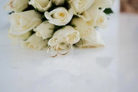 Two gold wedding rings in front of a bouquet of white roses Stock Photos