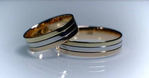 Two gold wedding rings lying on white-gray surface shining with light close up Stock-Footage 77079191