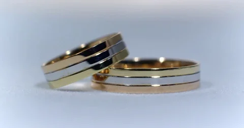 Two gold wedding rings lying on white-gray surface shining with light close up Stock Footage 77079473
