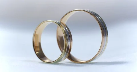 Two gold wedding rings lying on white-gray surface shining with light close up Stock-Footage 77079842