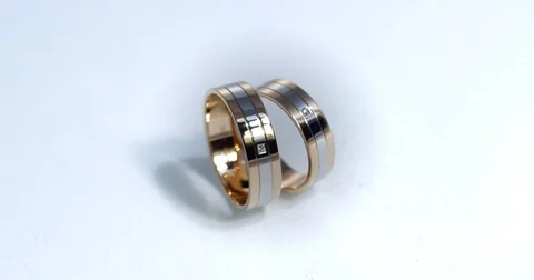 Two gold wedding rings lying on white-gray surface shining with light close up Stock Footage 77080648