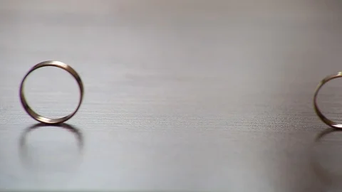 Two gold wedding rings rolling towards each other on a table Stock Footage 97955021