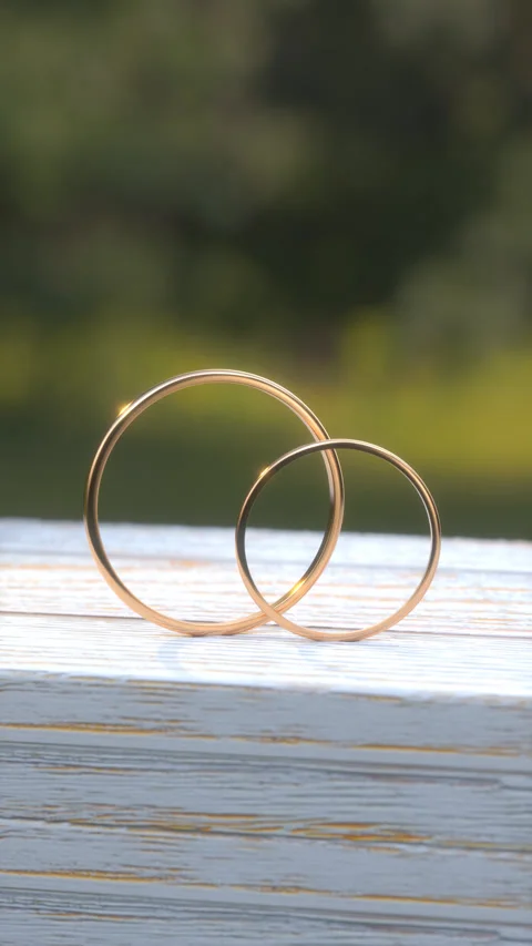 Two gold wedding rings stand on a white wooden table close-up. Stock Footage 250149152