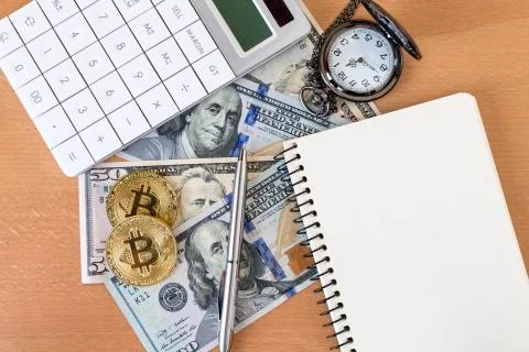 Two golden bitcoins, journal, pen, calculator, and pocket watch on us dollars Stock Photos