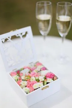 Two golden rings lying in flower box near wineglasses with champagne. Foto stock