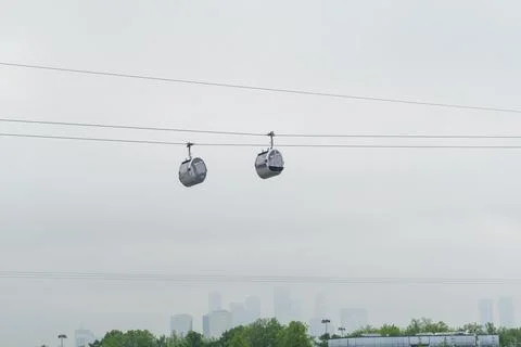 Two gondolas suspended on cables against a cloudy sky with a city skyline v.. Stock Photos