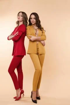 Two gorgeous models in colored suits and high heels over flat background. Stock Photos