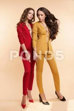 Two gorgeous models in colored suits and high heels over flat background. Stock Photos
