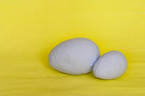 Two gray-colored eggs on a yellow plaster background. Stock Photos