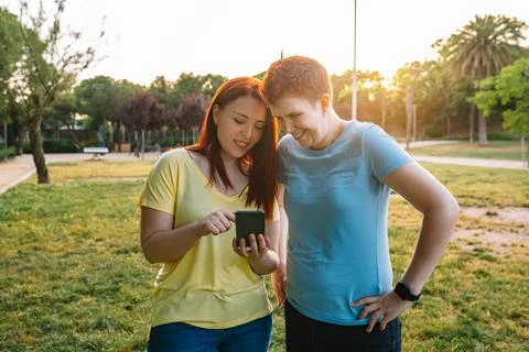 Two great friends looking at their smartphones while sharing a relaxing moment Stock Photos