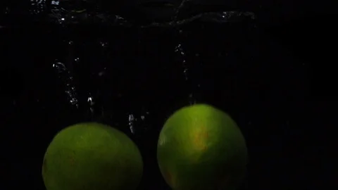 Two green lime are thrown into a container of water. Video of fruit in slow Stock Footage 105424517