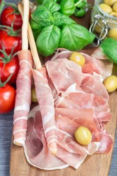 Two grissini bread sticks coiled with prosciutto ham on wooden board, vertica Foto stock