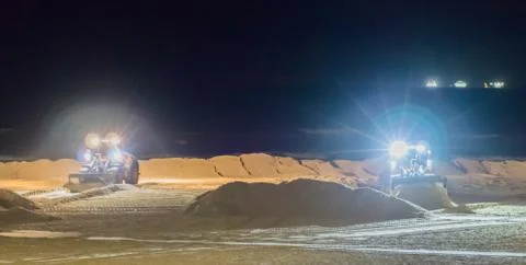 Two ground workers working at night in bulldozers at the beach moving the san Stock Photos