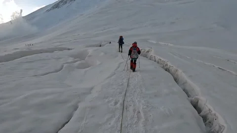 Two groups of climbers walk in bundles on a glacier past cracks at dawn 動画素材 208437693