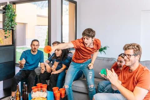 Two groups of young friends facing each other watching a sports championship Stock Photos
