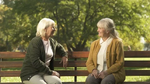 Two grumpy old ladies judging passerby people, sitting on bench in park, pension Stock Footage 100179087