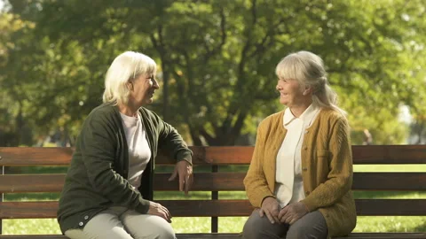 Two grumpy old ladies judging passerby people, sitting on bench in park, pension Stock Footage 100200306