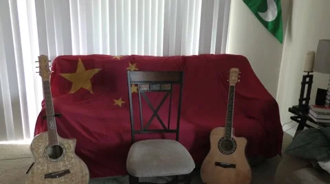 Two Guitars in room with Chinese Flag over couch and an empty chair Stock Footage 66182916