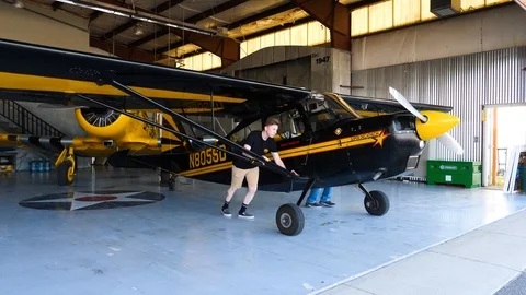 Two guys are pushing piston single Champion decathlon plane out of the hangar Stock Footage 115603204