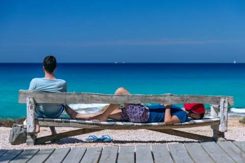Two guys are resting on a bench on the background of a calm blue sea Stock Photos