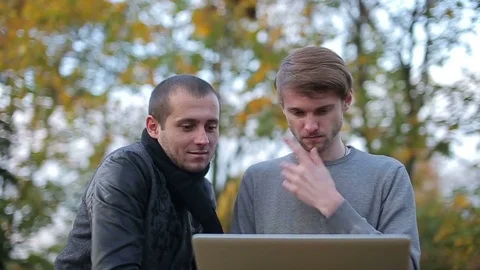 Two guys are sitting on a bench and open laptop talking and write - friends Video stock 70430400