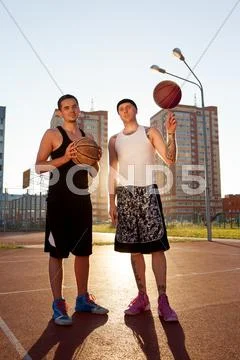 Two Guys Are Standing On The Basketball Court With Balls And Looking At The