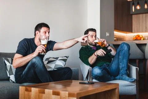 Two guys drinking beer watching sports on TV Stock Photos